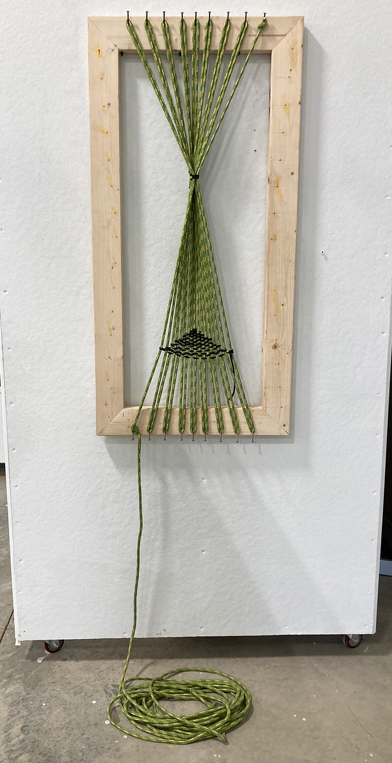 Abstract sculpture that consists of wooden frame, nails on opposite ends, and cord woven between nails and hanging to the ground