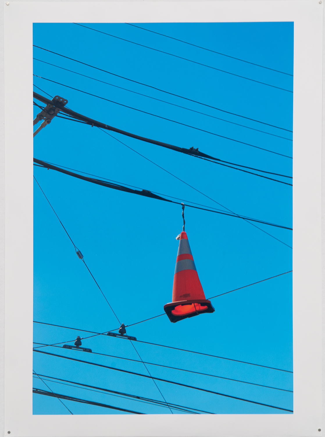 Image of an orange traffic cone hanging from electrical wires; inkjet print on matte paper