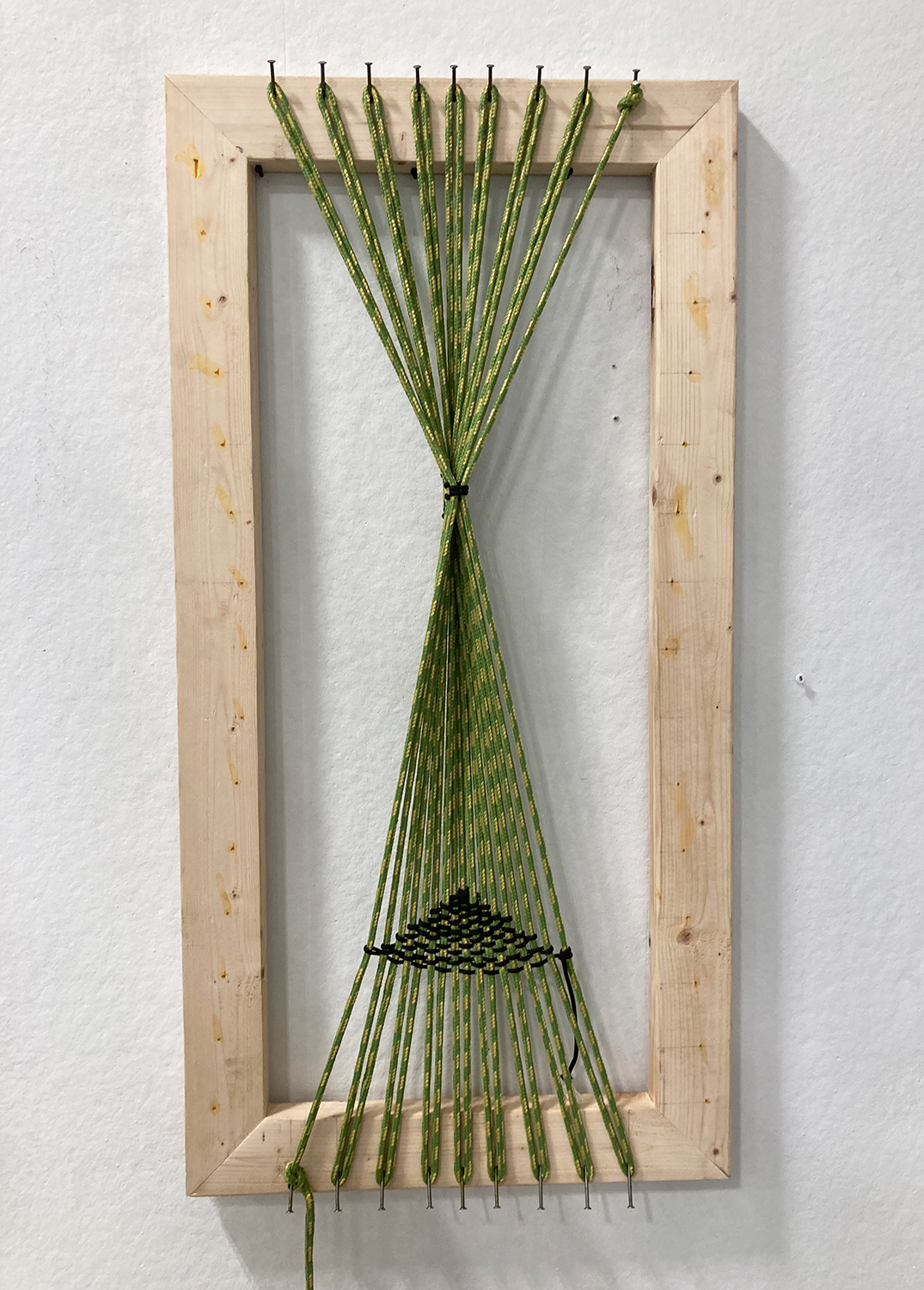 Close up of abstract sculpture that consists of wooden frame, nails on opposite ends, and woven cord