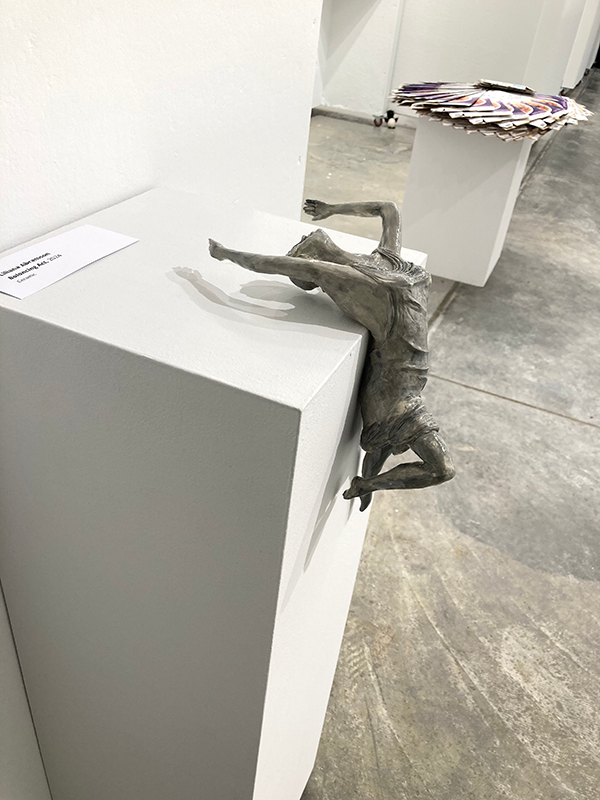 Ceramic sculpture of a girl balancing on back along the edge of a pedestal.