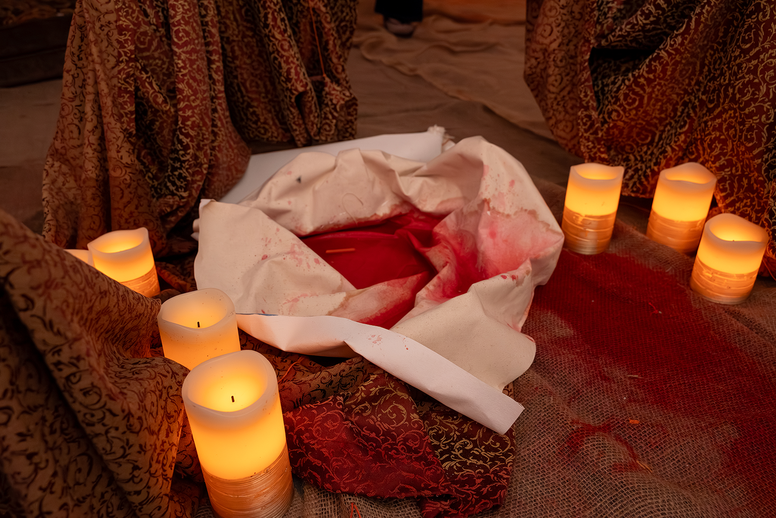 Close up of a puddle of red dye surrounded by pillows and fake lit candles