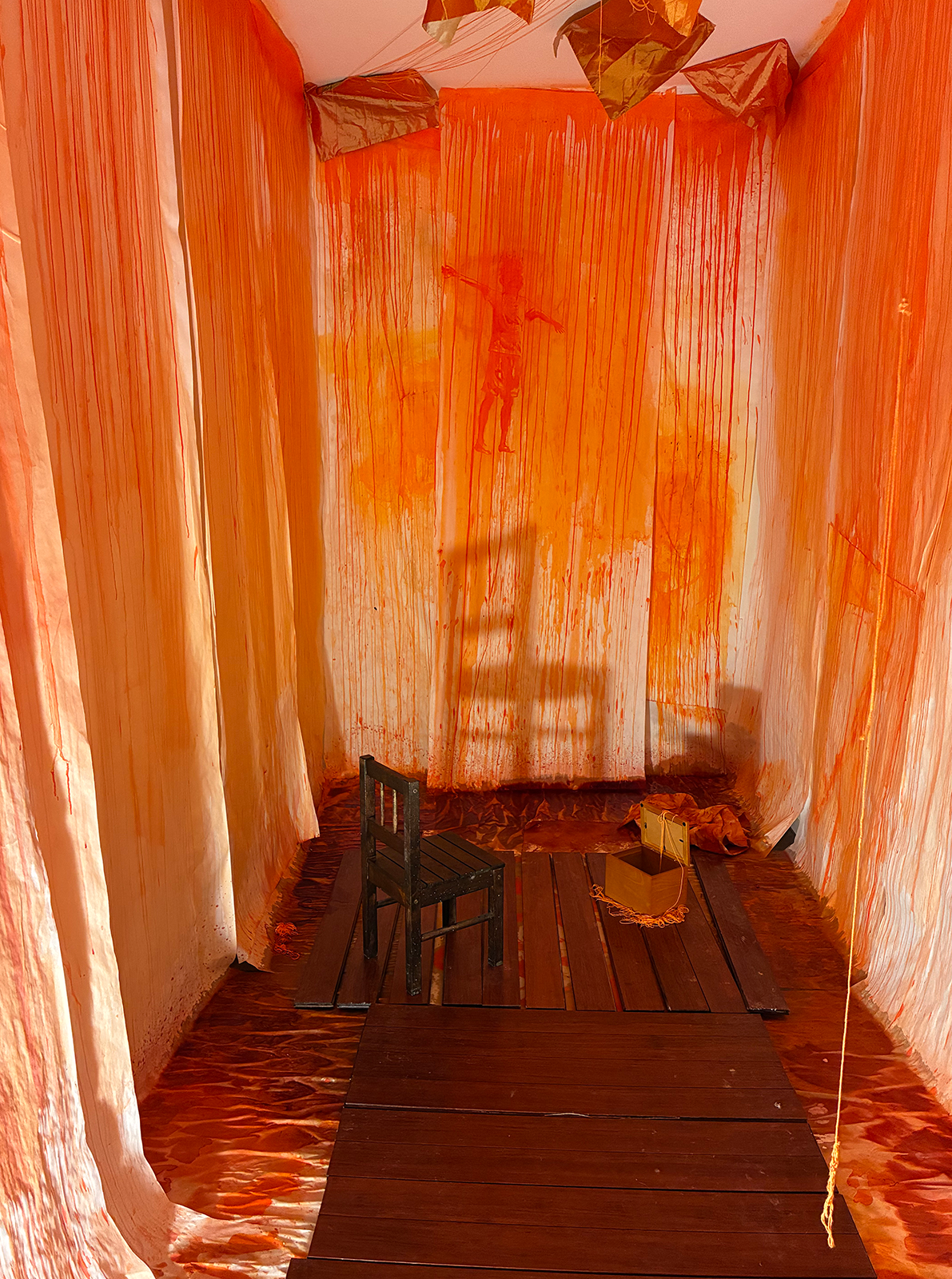 A chair uplit casting a shadow on the wall, with red dye all over the surrounding walls, and red material on the cieling 