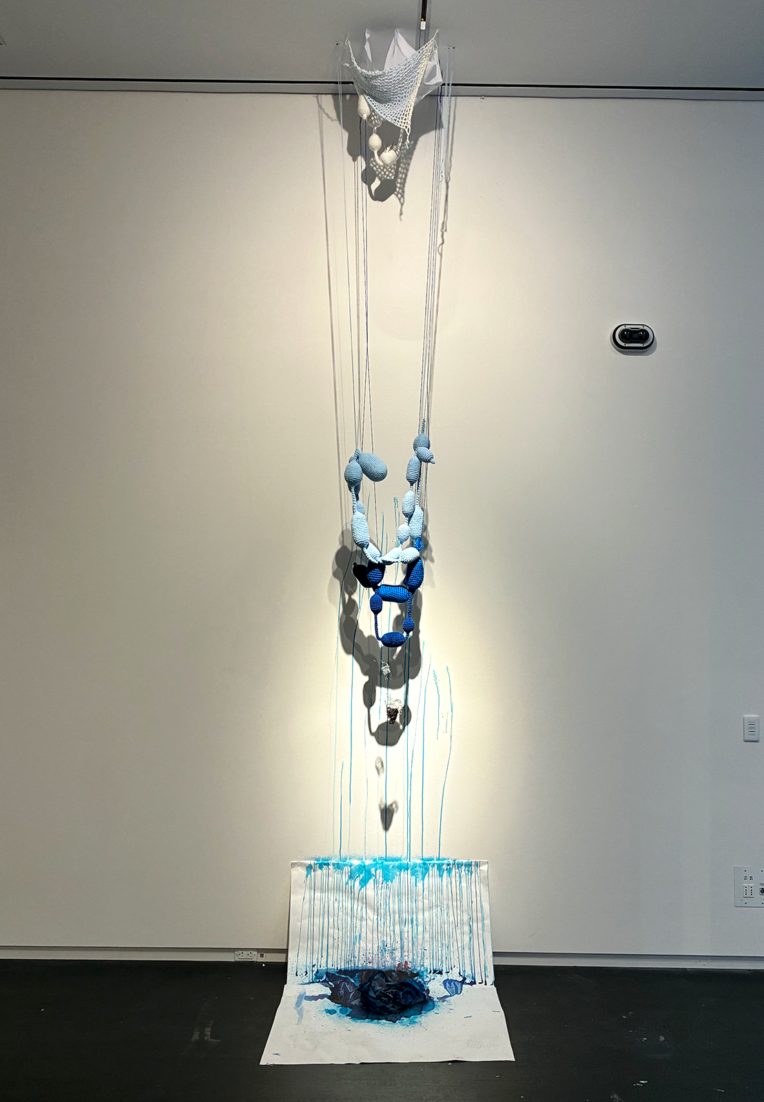 Image of yarn sculpture hanging from ceiling that drops into a puddle of blue dye